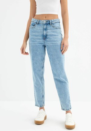 Jeans de tiro alto en azul claro con un diseño de pierna recta, que cuentan con cinco bolsillos y un cierre de botón. Combinados con zapatillas blancas.