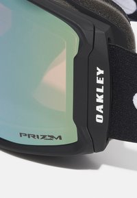 Zwarte skibril met een groen getinte lens, voorzien van een stevig frame, zachte schchuimvoering en een verstelbare elastische band met het Oakley-logo.
