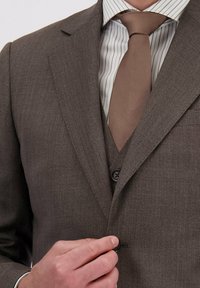 Man die een knoop dichtknopt van een bruine driedelige pak, gedragen over een gestreept overhemd met een effen bruine stropdas.