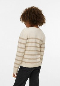 Pull beige à rayures avec une texture douce et un ourlet côtelé. Présente des rayures horizontales marron clair. Porté avec un jean noir.