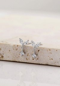 Pendientes de plata con un cristal en corte marquesa en la parte superior y un acento de cristal en corte cuadrado colgante, con un acabado metálico suave.