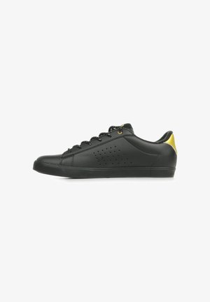 Sneaker bassa nera con lacci neri, pannello laterale traforato e dettaglio giallo sul tallone, mostrata di profilo su sfondo bianco.