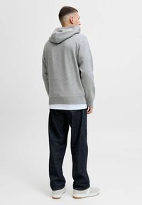 Gray hooded sweatshirt with a relaxed fit, ribbed hem, and cuffs, paired with dark denim pants and light-colored sneakers.