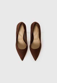 Brune semskede høyhælte sko med spiss tå-design. Innvendig er skoen beige med geometriske mønsterinnsatser.