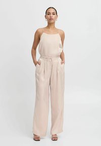 Lichtroze satijnen jumpsuit met dunne bandjes, wijde broekspijpen, elastische taille en zijzakken, met een gladde textuur en minimaal ontwerp.