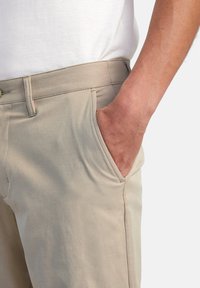 Beige pants with a smooth texture, featuring side pockets and visible stitching details, worn with a white t-shirt.