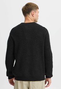 Black knitted sweater with a textured finish, crew neckline, and relaxed fit. Features long sleeves and side slits for ease of movement.