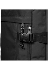 Black backpack featuring a sturdy fabric, double zip closure, and a clip buckle. Includes a textured strap and decorative stitching details.