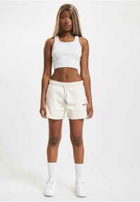 Cream cotton shorts with an elastic waistband, paired with a white ribbed crop tank top. White sneakers and knee-high white socks complete the look.