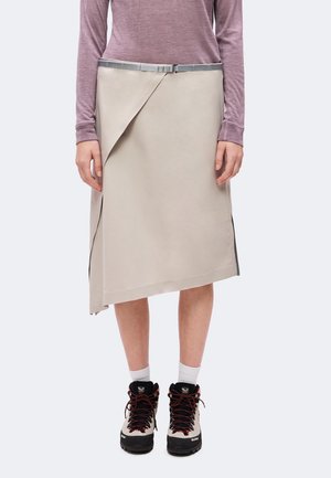 Personne portant une jupe portefeuille beige avec une ceinture argentée, un haut mauve à manches longues, des chaussettes blanches et des chaussures de randonnée beige et noires.