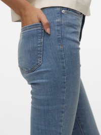 Hand resting inside the back pocket of fitted blue denim jeans with visible stitching and rivets.