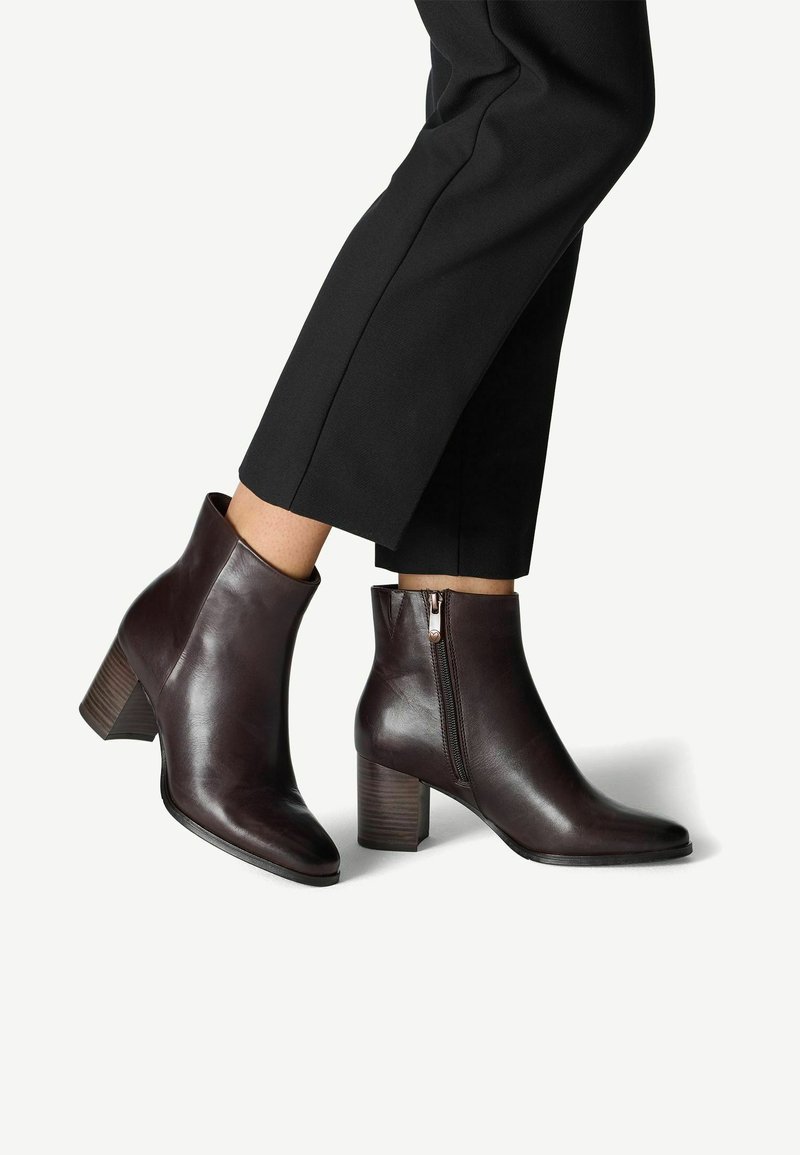 Bottines en cuir brun foncé avec un bout pointu, une fermeture éclair sur le côté et un talon empilé. Texture lisse et détails de design minimal.