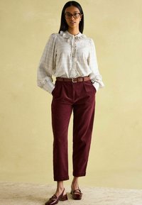 Weißes kariertes Blusenshirt mit Rüschennetz, burgunderfarbene Cordhosen und dunkle burgunderfarbene Schuhe mit niedrigem Absatz. Brauner geflochtener Gürtel.