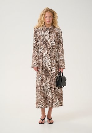 Leopard print dress with long sleeves, collar, and a tie waist. The model holds a black handbag and wears black sandals. Smooth fabric texture.