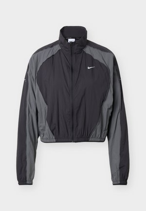 Veste légère zippée Nike noire et grise avec col haut, manches longues, poignets élastiques, et petit logo blanc sur la poitrine gauche.
