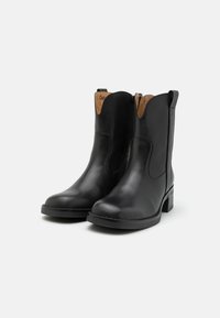 Botas de cuero negro hasta el tobillo con un diseño cosido, cremallera lateral y un tacón bajo y grueso. El interior cuenta con un forro en contraste de color marrón claro.