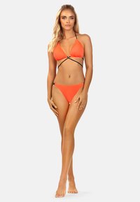 Jasnopomarańczowy bikini z trójkątnym stanikiem z czarnymi elementami i cienkimi ramiączkami, w komplecie z dopasowanymi, niskimi majtkami.