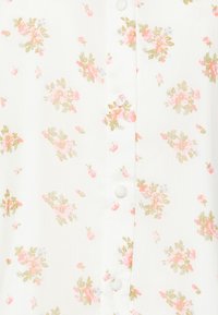 Camicia a maniche corte con bottoni, caratterizzata da uno sfondo bianco con fiori rosa pastello e verdi, e bottoni bianchi tondi lungo la parte anteriore.
