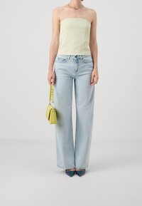 Haut léger jaune sans bretelles avec un design ajusté, associé à un jean large taille haute bleu clair. Petit sac à main jaune, chaussures pointues bleues.