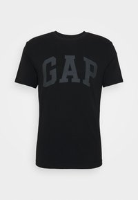 Camiseta de algodón negra con un gran logo gris de "GAP" en el pecho. Cuello redondo clásico y mangas cortas, textura suave.