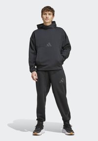 Black athletic hoodie with a high neck, front pocket, and elastic cuffs. Paired with matching joggers featuring subtle branding accents.