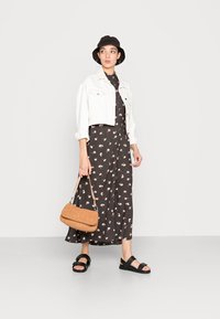 Abito floreale nero con collo alto, giacca di jeans bianca cropped, cappello a secchiello nero, borsa marrone e sandali neri. Materiali testurizzati visibili.