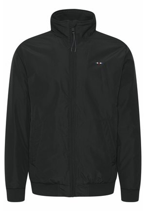 Čierna vetrovka s vysokým golierom, zipsovým uzatváraním a dvoma bočnými vreckami. Obsahuje malé vyšívané logo v červenej, bielej a modrej farbe.