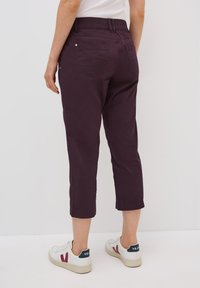 Pantaloni cropped viola scuro con vita elasticizzata, dotati di tasche posteriori e una texture liscia, abbinati a sneakers bianche.