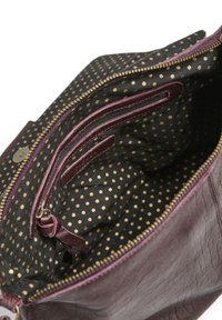 Intérieur d'un sac en cuir bourgogne foncé avec un tissu noir parsemé de pois dorés. Comprend des poches zippées et des compartiments fendus pour une meilleure organisation.