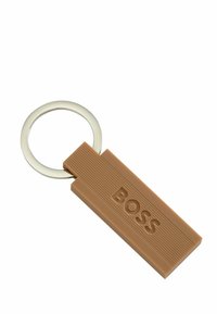 Breloczek wykonany z brązowego gumowego materiału o żłobionej fakturze, z wytłoczonym napisem "BOSS", przymocowany do srebrnego metalowego pierścienia.