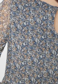 Blusa floral confeccionada en un tejido ligero y transparente con un patrón multicolor en tonos azul, verde y marrón. Cuello redondo y mangas cortas.