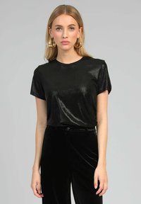 Chemise noire à manches courtes en tissu brillant et lisse avec un col rond, assortie à un pantalon en velours noir taille haute.
