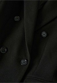 Manteau en laine noire avec quatre boutons noirs brillants disposés en style croisé, montrant une partie du col et du revers.