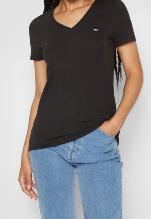 T-shirt nera a maniche corte con scollo a V realizzata in tessuto morbido. Presenta un piccolo logo sul petto e un orlo leggermente curvo.