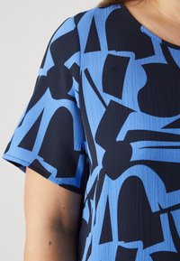 Μπλε και μαύρος μπλούζα με σχέδιο, κοντά μανίκια, με αφηρημένο σχέδιο και υφή. Στρογγυλή λαιμόκοψη και άνετη εφαρμογή.