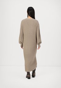Lång, beige stickad klänning med ribbad textur, med puffärmar och en avslappnad passform, tillsammans med knähöga mörkbruna stövlar.