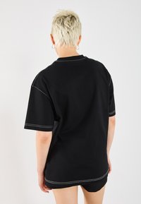 Black oversized t-shirt made of cotton, featuring contrasting white stitching along seams and neckline, with short sleeves and a relaxed fit.