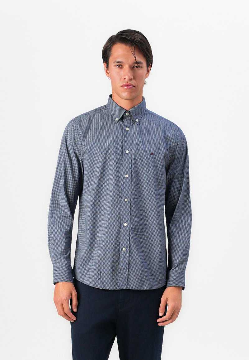 Camisa de botones navy con un pequeño patrón de lunares blancos, mangas largas, cuello punto y un logo sutil de la marca en el pecho.