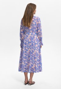 Robe à manches longues en tissu léger avec un motif floral bleu et rose. Silhouette évasée avec une ceinture à la taille et des poignets à boutons.