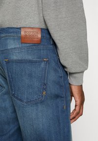 Modré denimové džíny s koženou nášivkou Scotch & Soda, které mají jedinečné prošívání na zadních kapsách a rovný střih nohavic.