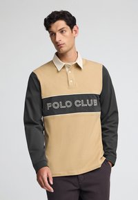 Beżowa i ciemnoszara koszula polo z długim rękawem, z kremowym kołnierzykiem, z trzema guzikami z przodu oraz haftem "POLO CLUB" na piersi.
