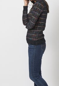 Multikleurige gebreide trui in zwart met horizontale streep patronen. Fluffy textuur en geribde manchetten. Gecombineerd met donkerblauwe spijkerbroek.