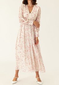 Vestido de manga larga y escote en V, hecho de una tela ligera y transparente con patrones de hojas rosas sobre un fondo blanco. Presenta una cintura fruncida y una silueta fluida.