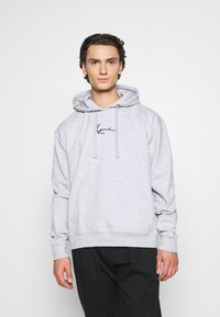 Szara bluza z kapturem wykonana z miękkiego materiału, wyposażona w kieszeń z przodu, regulowany sznurek i minimalistyczne czarne logo na piersi.