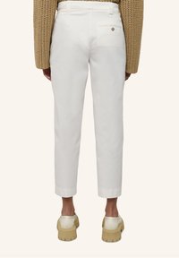 Pantalon en coton blanc à jambe droite avec un ourlet retroussé, doté d'une poche arrière avec un bouton. Associé à des chaussures à plateforme beiges.