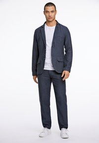 Mörkblå kavaj och matchande byxor i strukturerad väv, kombinerade med en enkel vit t-shirt och vita sneakers.