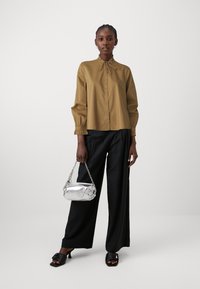 Chemise à col brun avec des manches élastiques, associée à un pantalon large noir et un sac à chaîne argentée. Sandales à talons noires.