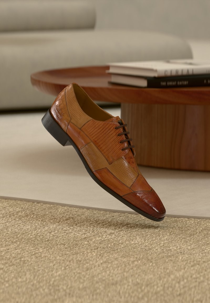 Chaussure habillée en cuir marron à lacets avec texture patchwork flottant au-dessus d'un tapis beige tissé dans un cadre de salon.