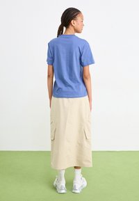 Tricou din bumbac de culoare albastru deschis, cu mâneci scurte, asortat cu o fustă bej până la genunchi, cu buzunare laterale și o textură netedă. Adidașii argintii completează ținuta.