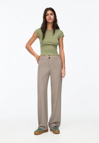 Top court vert ajusté, pantalon large beige, et baskets teal avec semelles brunes. Comprend une fermeture à bouton et un design à jambes droites.